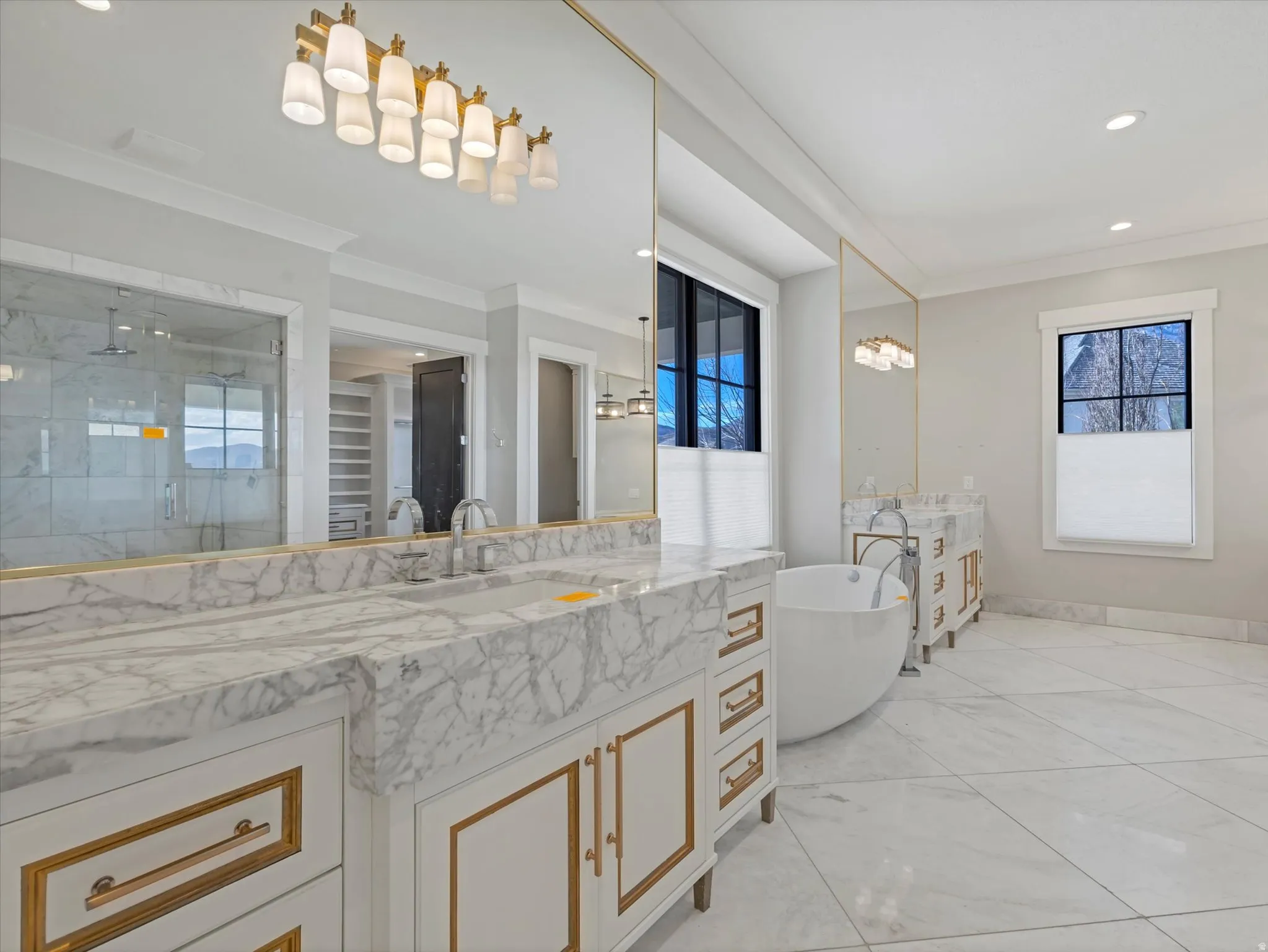 Primary bathroom featuring two vanities, a shower stall, ornamental molding, a spacious closet, and a soaking tub