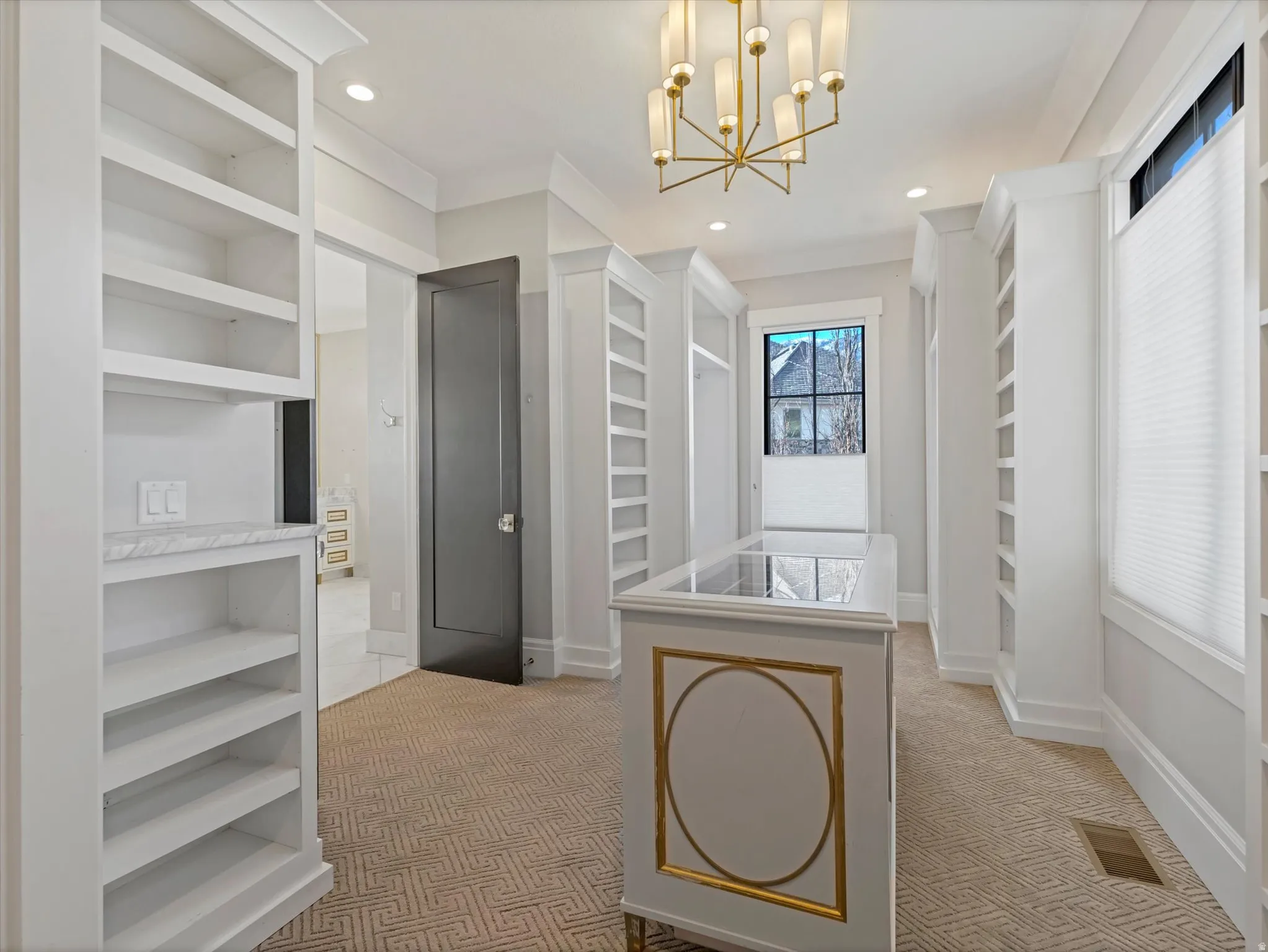 Primary bedroom walk in closet with light colored carpet and a chandelier