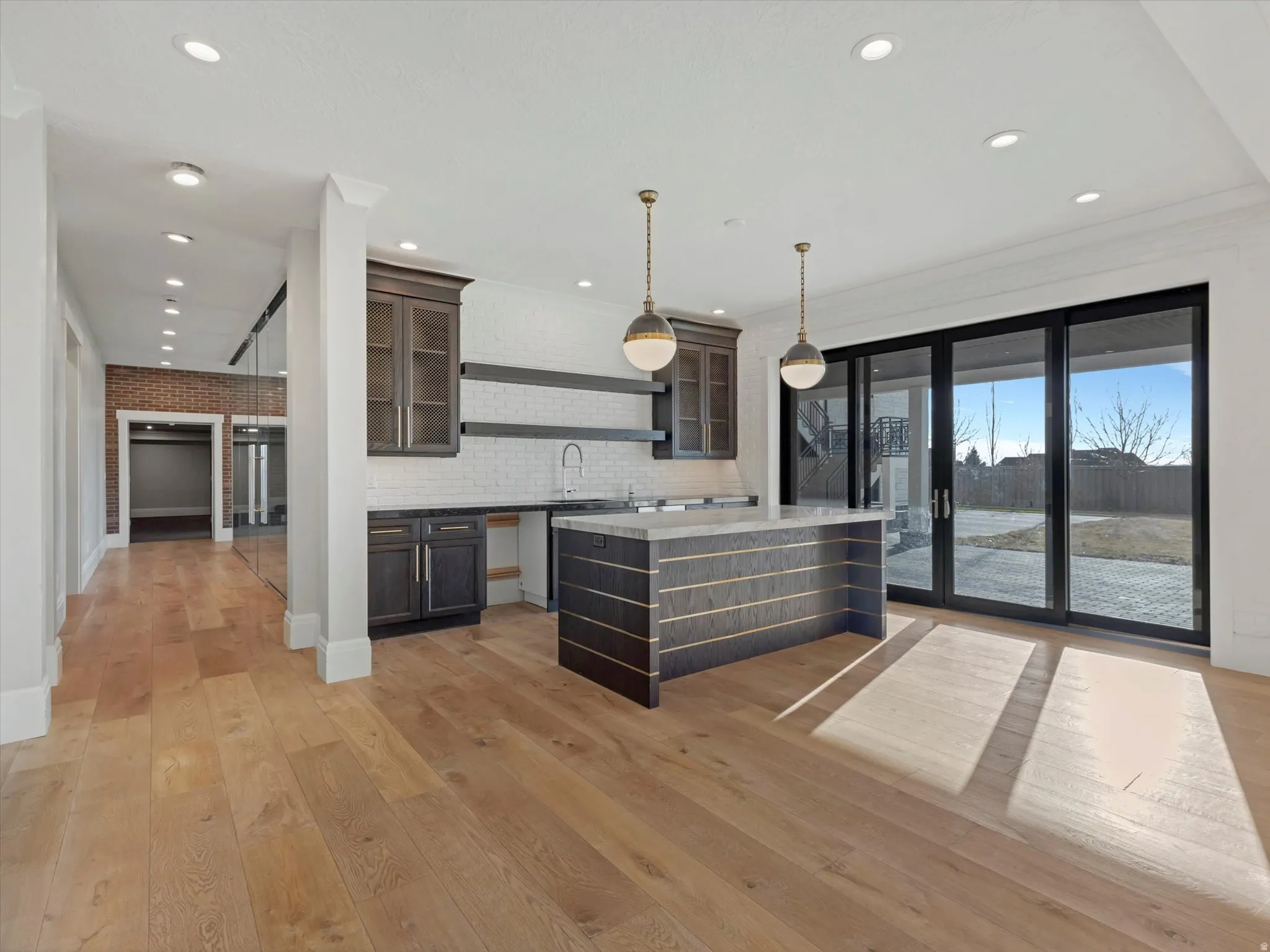Walkout kitchen with open shelves, decorative light fixtures, glass insert cabinets, light wood-style flooring, and ornamental molding