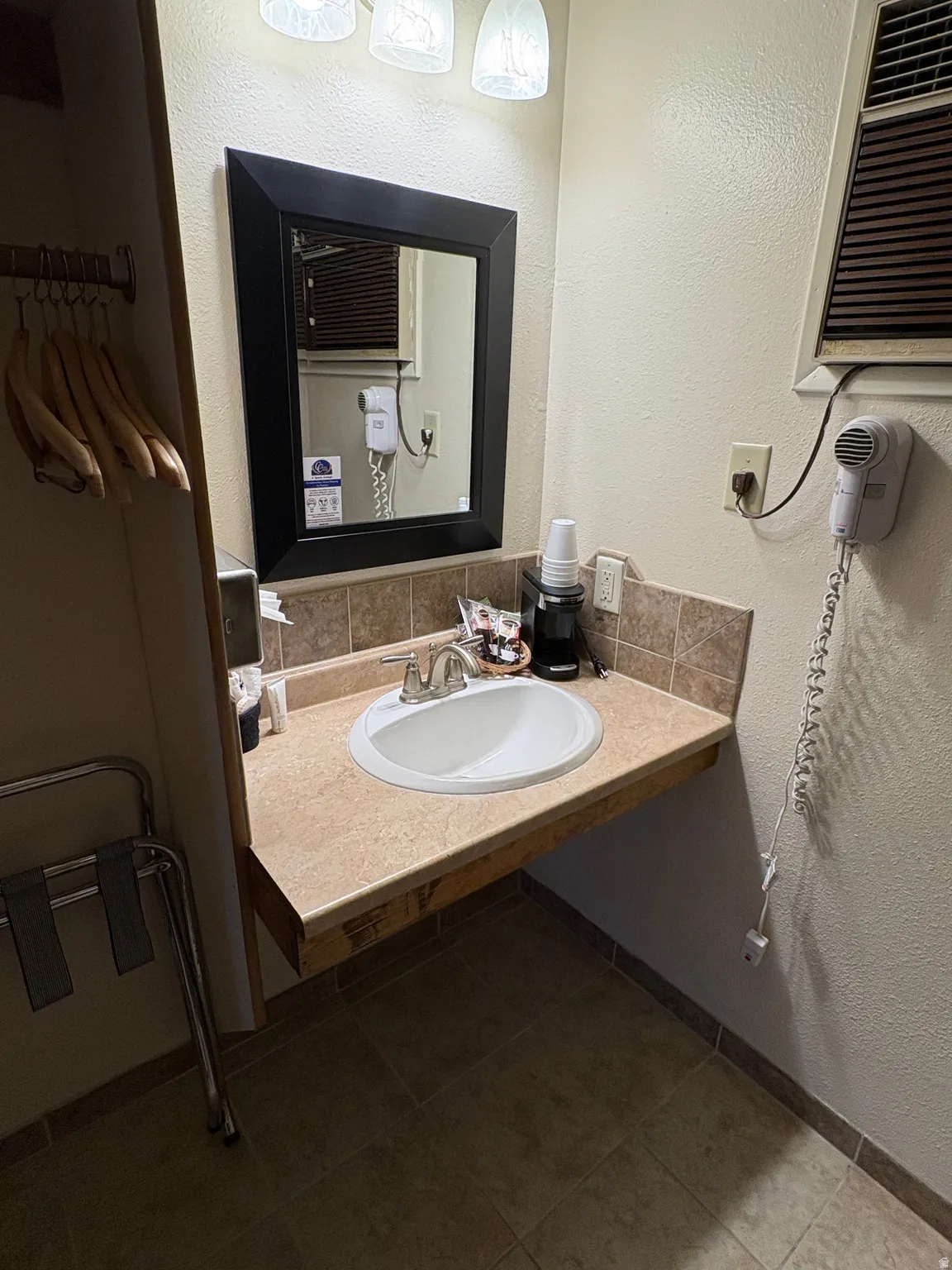 Bathroom featuring a textured wall, decorative backsplash, vanity, and dark tile patterned floors