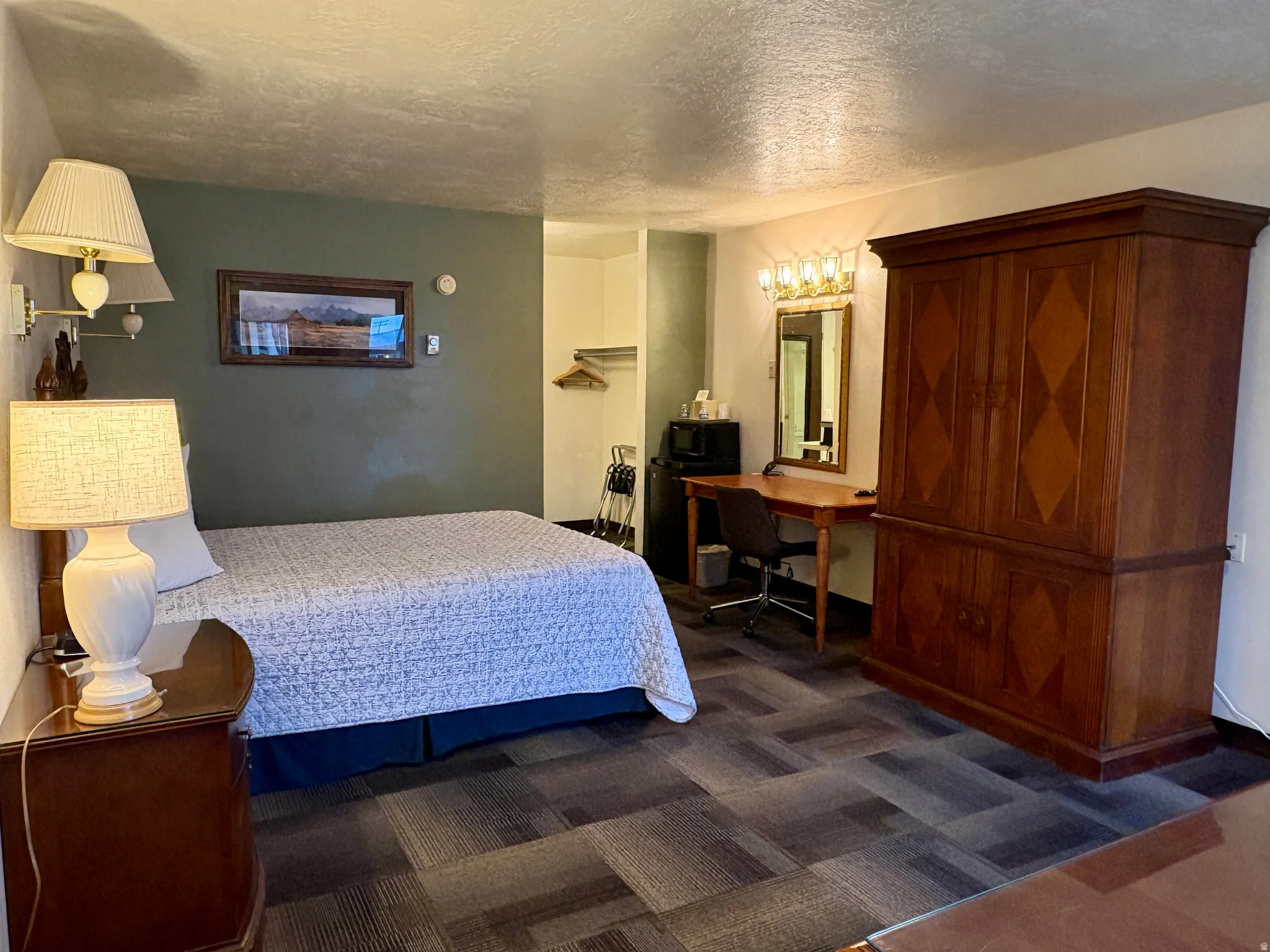 Bedroom with a textured ceiling, dark carpet, and an office area