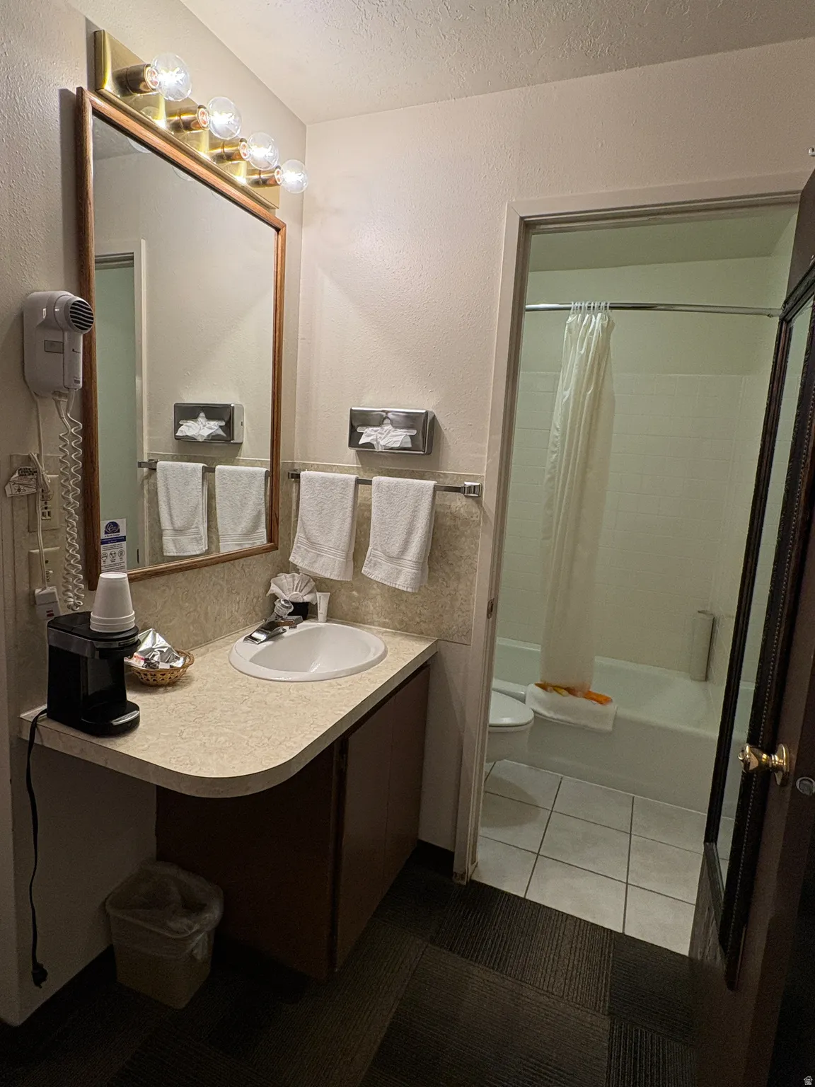Full bath featuring a textured ceiling, shower / bath combination with curtain, vanity, a textured wall, and light tile patterned floors