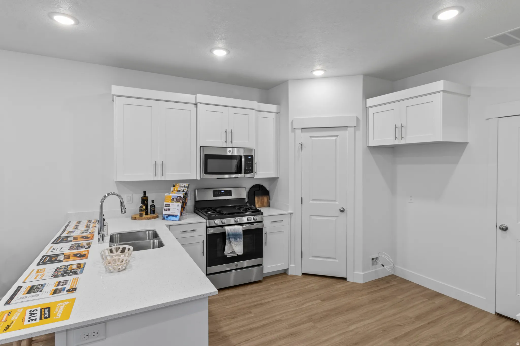 Kitchen with a peninsula, stainless steel appliances, white cabinetry, light wood-type flooring, and recessed lighting