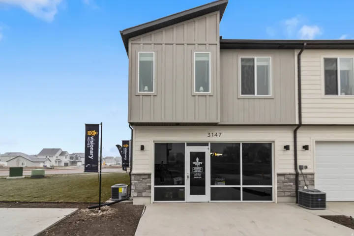 Rear view of property featuring stone siding, board and batten siding, an attached garage, concrete driveway, and a yard