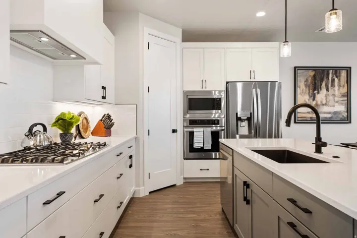 Kitchen featuring stainless steel appliances, decorative light fixtures, dark wood-style flooring, light stone counters, and dual tone cabinets