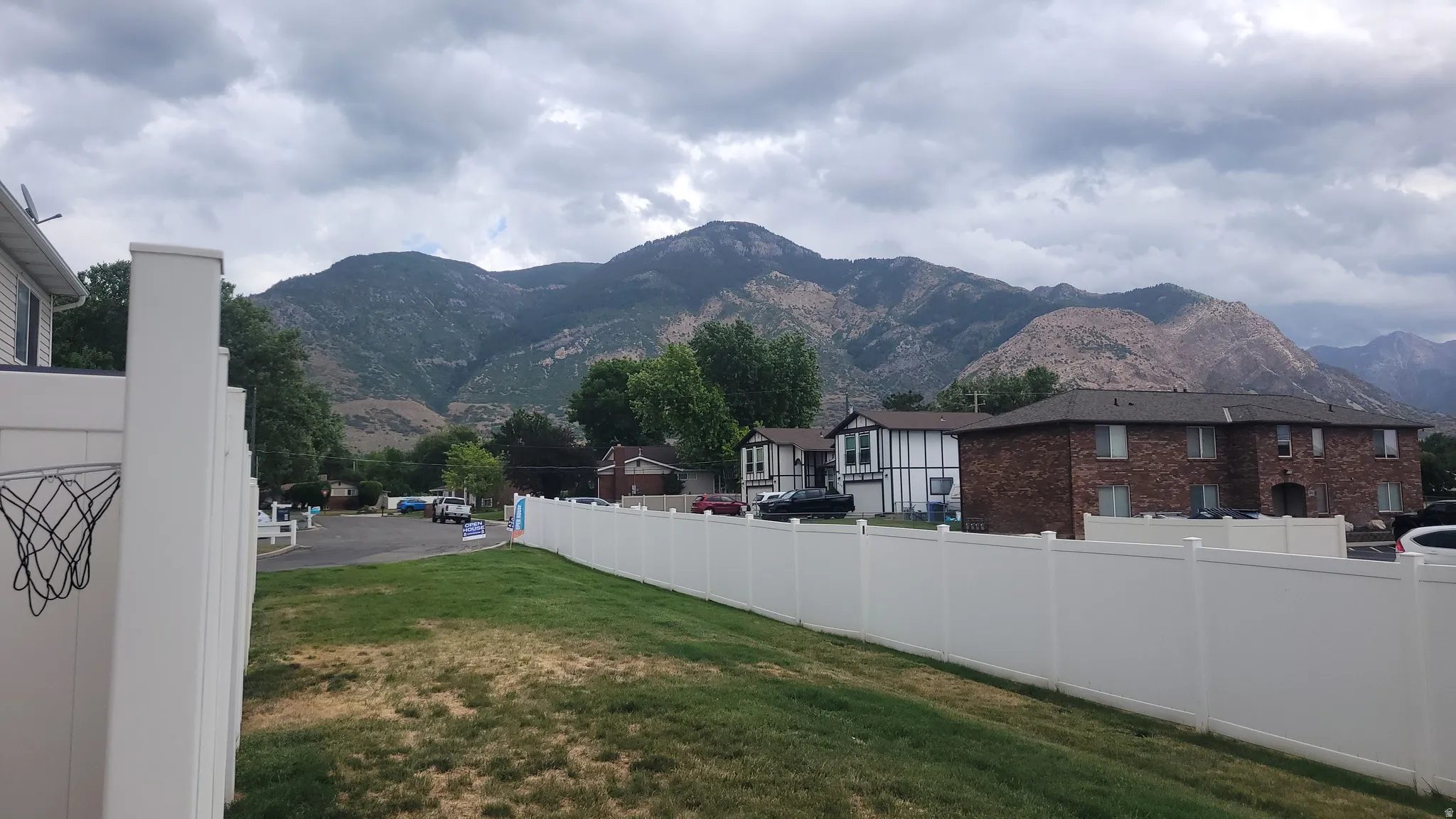 Expansive mountain backdrop with a manicured lawn and a durable white privacy fence
