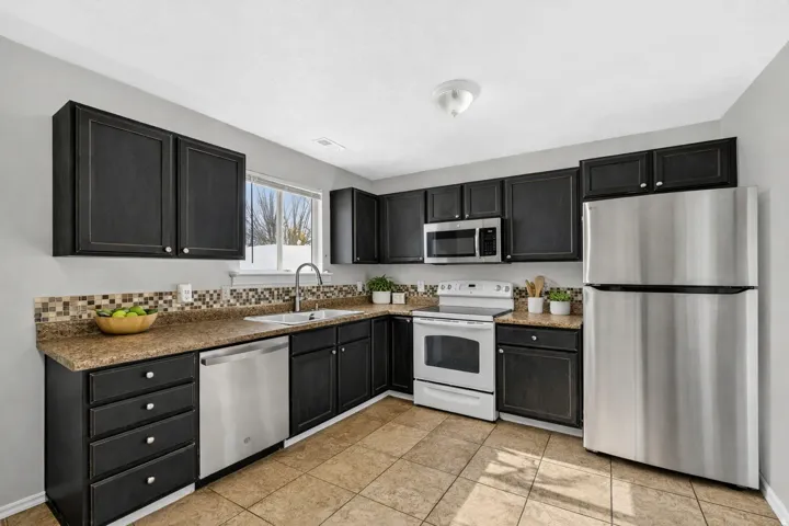 Kitchen featuring dark cabinetry, tile backsplash, stainless steel appliances, and tile flooring