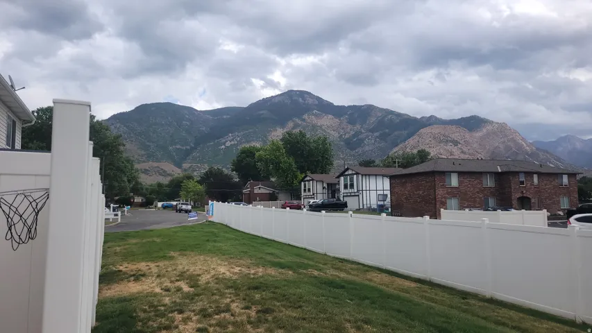 Expansive mountain backdrop with a manicured lawn and a durable white privacy fence