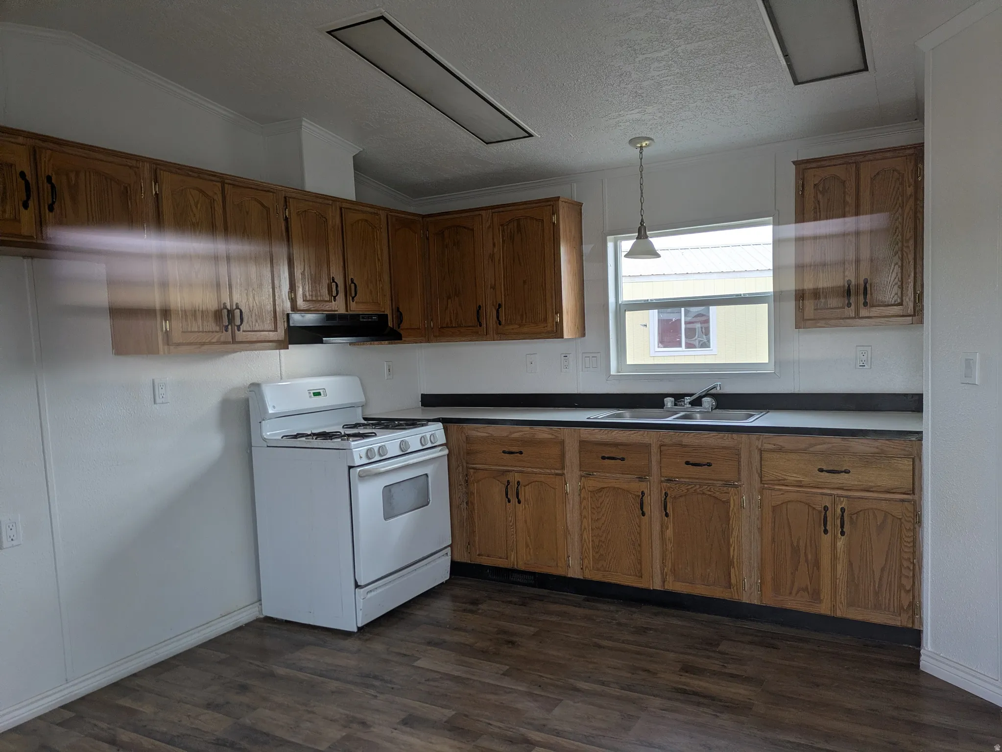 Kitchen featuring pendant lighting, white gas range oven, wood finish cabinets, dark wood-type flooring, and ornamental molding