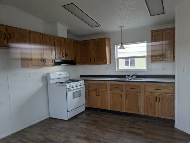 Kitchen featuring pendant lighting, white gas range oven, wood finish cabinets, dark wood-type flooring, and ornamental molding