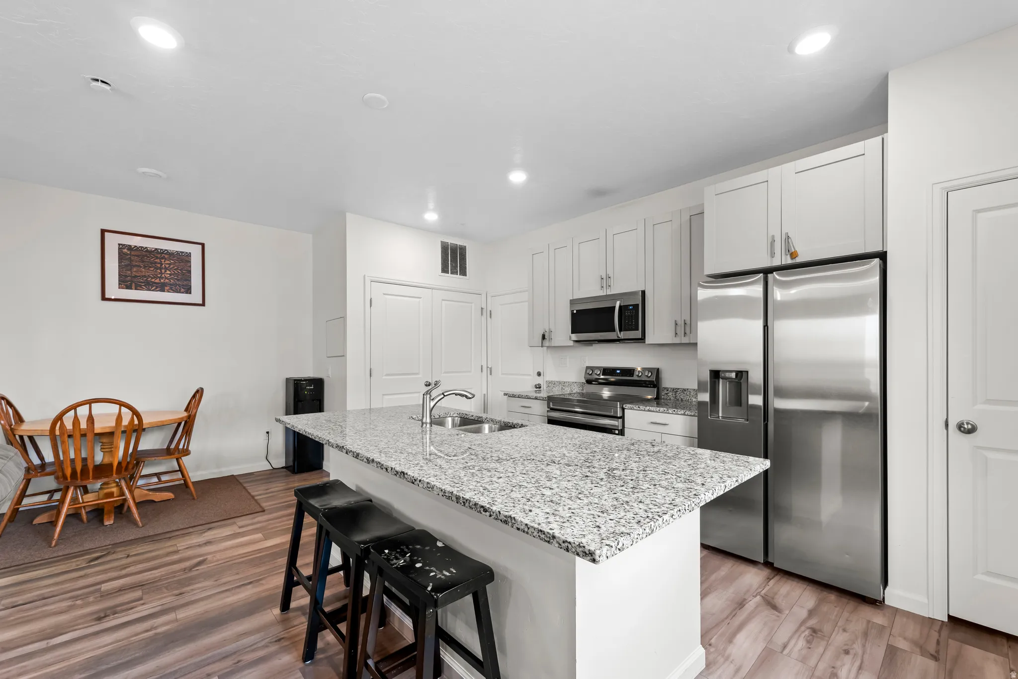 Kitchen featuring stainless steel appliances, light stone counters, a center island with sink, light wood-style flooring, and a breakfast bar