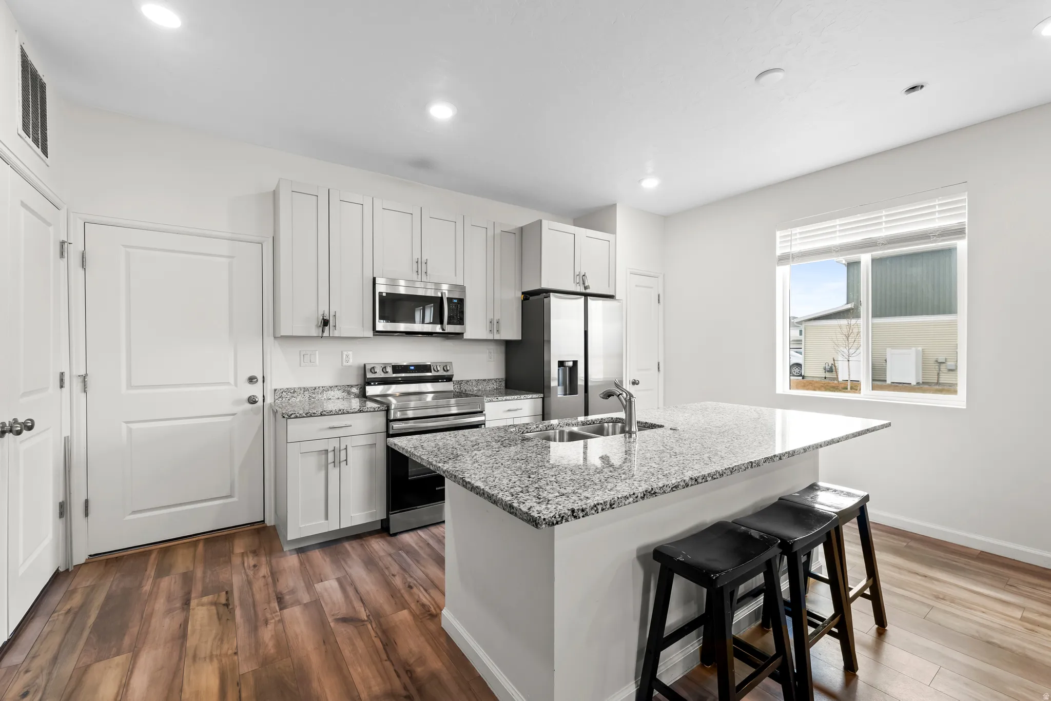 Kitchen featuring light stone counters, a kitchen breakfast bar, stainless steel appliances, a center island with sink, and dark wood-style flooring