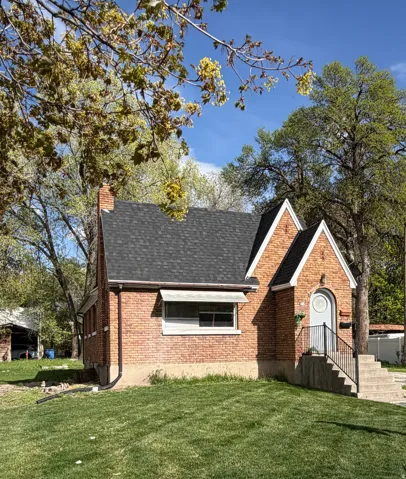 View of front of house featuring a front lawn, roof with shingles, brick siding, and a chimney