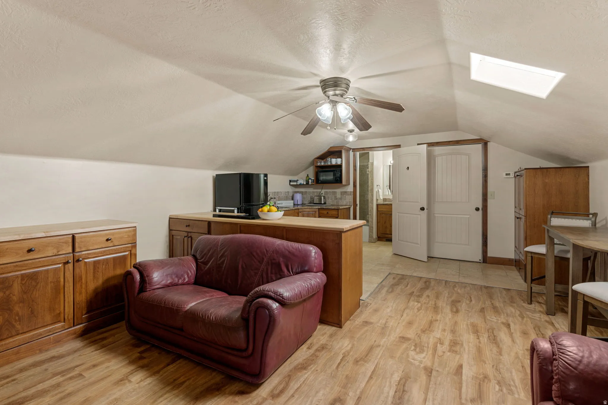 ADU Greatroom w/ light wood finished floors, a ceiling fan, and a skylight