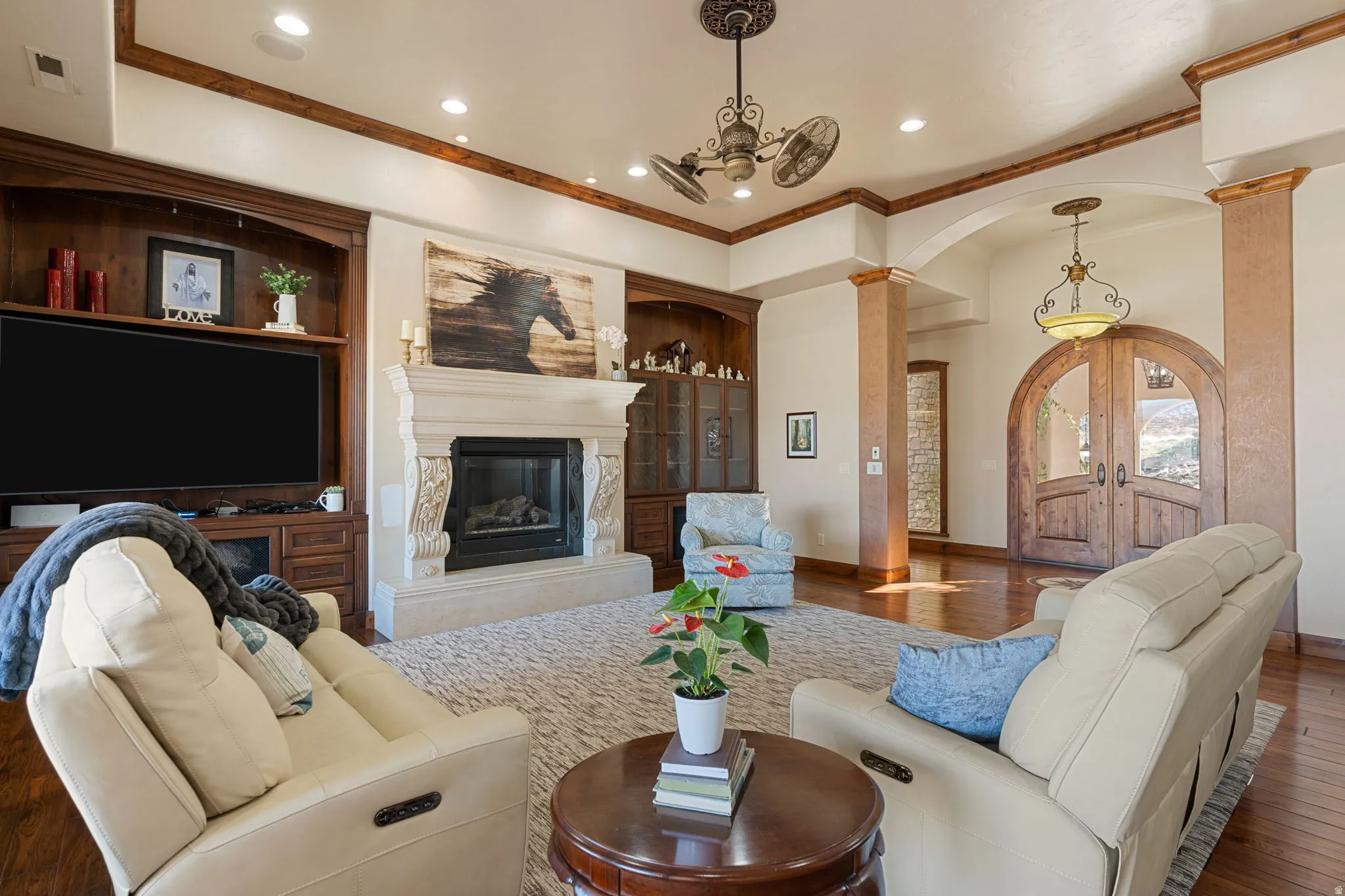Living area featuring arched walkways, hardwood / wood-style floors, ornamental molding, a premium fireplace, and hanging lights
