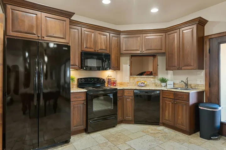 Kitchen featuring black appliances, stone tile floors, light stone counters, and recessed lighting