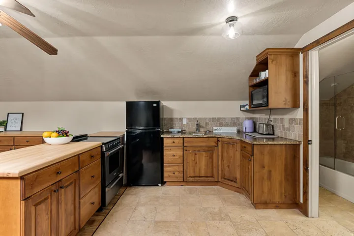 ADU Kitchen featuring wood finish cabinetry, black appliances, open shelves, a peninsula, and tasteful backsplash