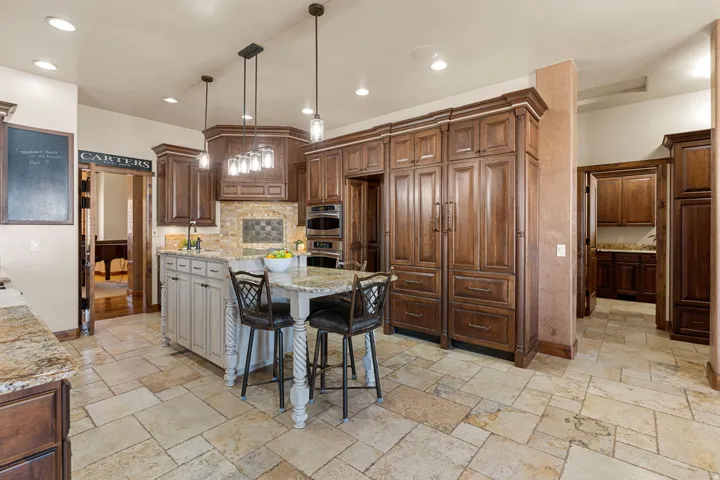 Kitchen featuring a breakfast bar, hanging light fixtures, a kitchen island, light stone countertops, and stone tile flooring