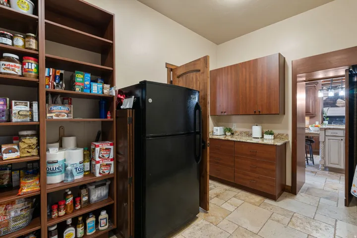 Kitchen with stone tile floors, freestanding refrigerator, light stone counters, and wood finish cabinetry