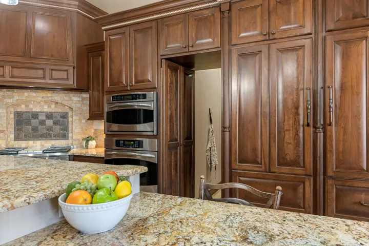 Kitchen featuring light stone counters, decorative backsplash, double oven and HIDDEN PANTRY
