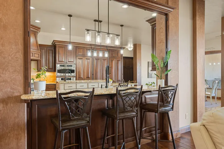 Kitchen with light stone counters, decorative light fixtures, wood finish cabinets, dark wood-style floors, and a breakfast bar area
