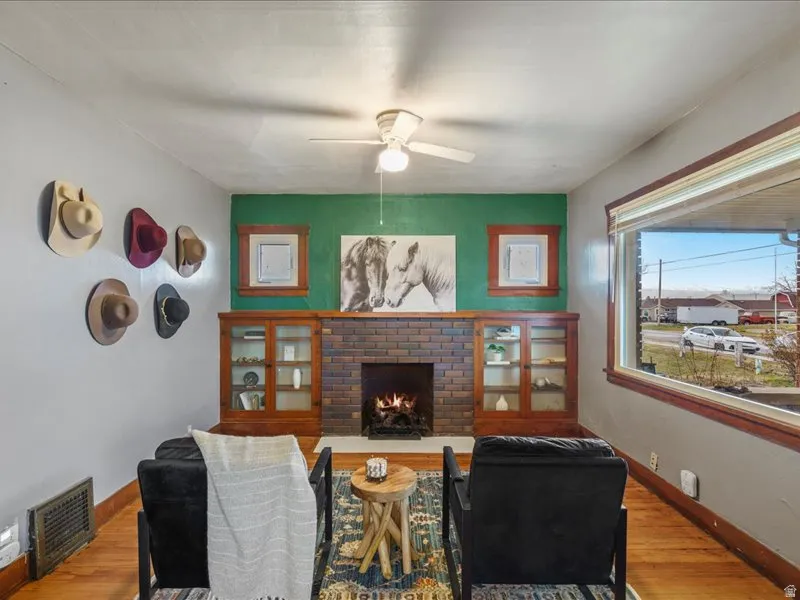 Living area with wood finished floors, a ceiling fan, and a brick fireplace