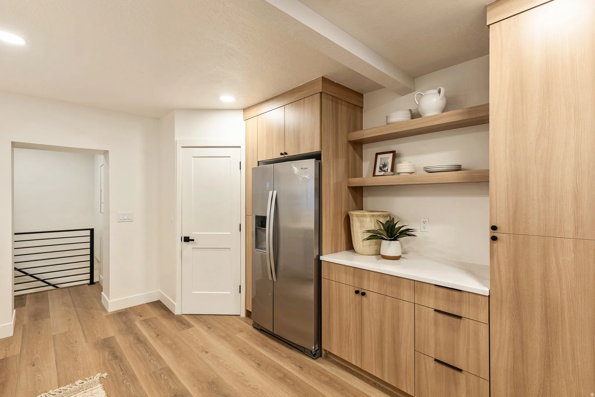 Kitchen featuring modern cabinets, stainless steel fridge with ice dispenser, open shelves, light wood-style floors, and light wood finish cabinets
