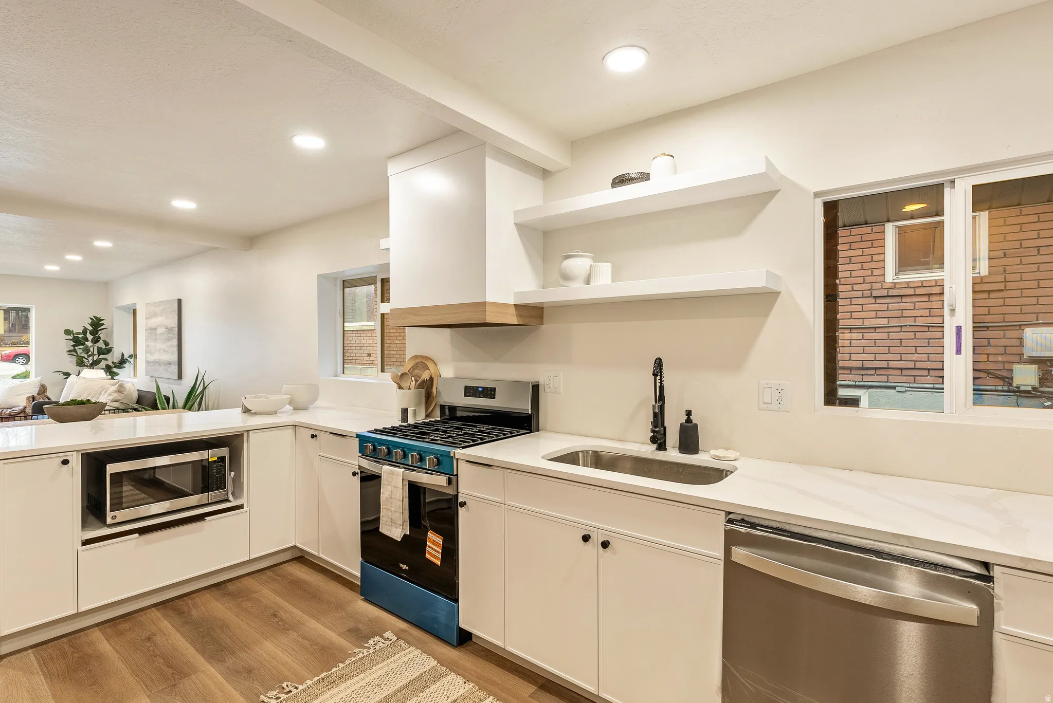 Kitchen with stainless steel appliances, open shelves, light wood-style flooring, light stone countertops, and white cabinetry
