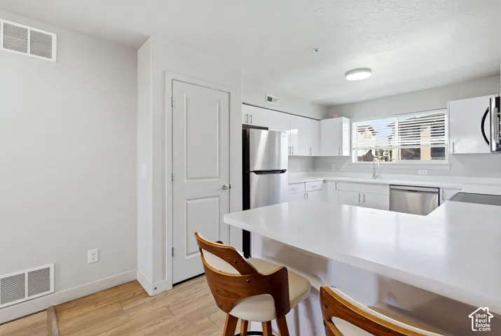 Kitchen featuring white cabinetry, stainless steel appliances, solid-surface countertops with a breakfast bar, and wood-finish flooring