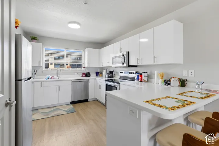 Kitchen featuring white high-gloss cabinetry, white solid-surface countertops, wood-finish flooring, stainless steel appliances, and an integrated breakfast bar