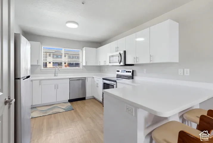 Kitchen featuring white flat-panel cabinetry, solid-surface countertops, wood-finish flooring, and stainless steel appliances