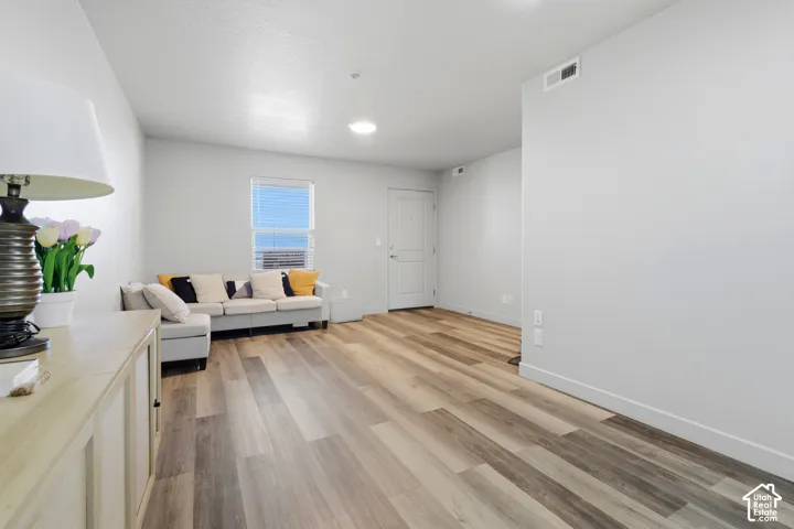 Neutral-toned interior featuring wood-finish flooring, a single-panel entry door, and a horizontal window with blinds