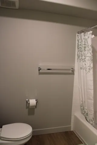 Full bath with shower / bath combination with curtain and dark wood-style floors