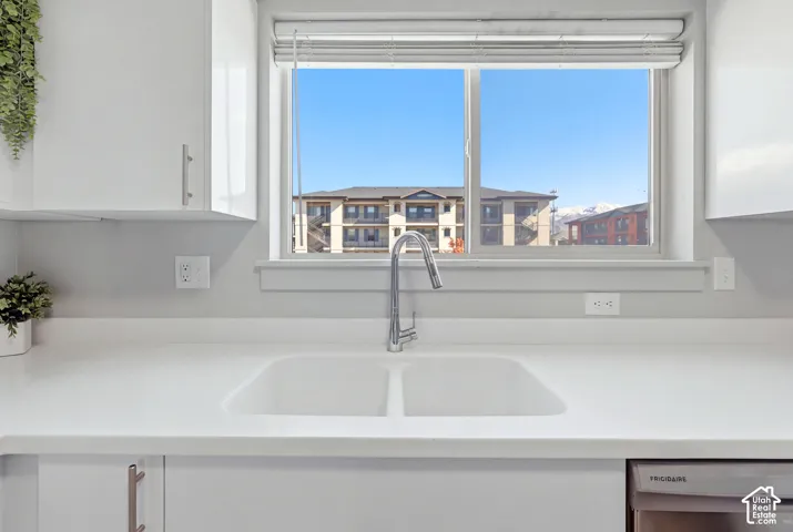 Modern kitchen featuring a sleek white quartz countertop with an undermount double-basin sink, polished chrome gooseneck faucet, and expansive window framing cityscape vistas