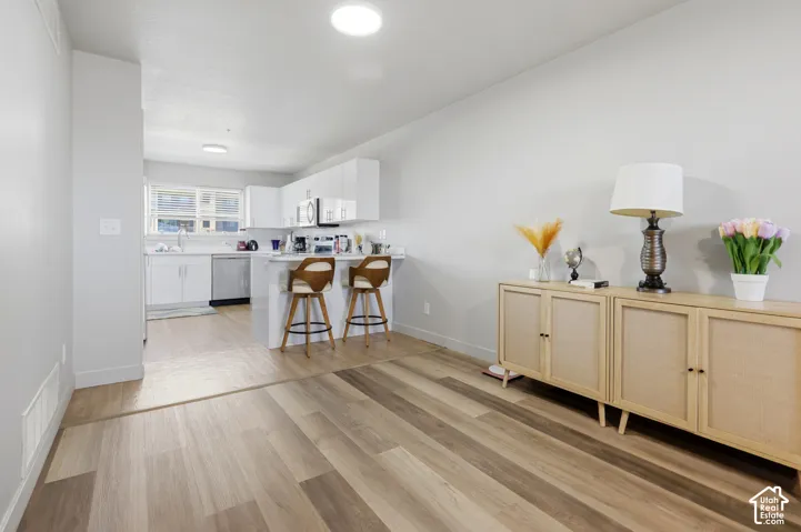 Kitchen featuring high-gloss white cabinetry, wood-finish flooring, and a breakfast bar