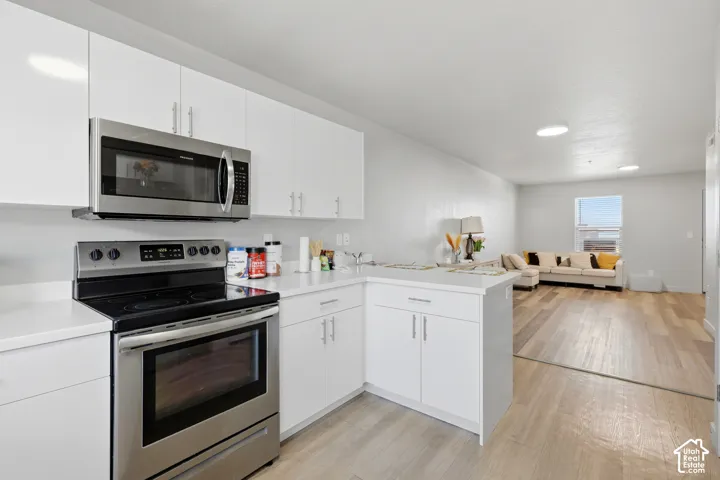 Kitchen featuring white cabinetry, stainless steel appliances, and solid surface countertops, paired with wood-finish flooring