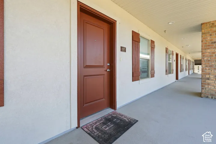 Exterior walkway featuring a covered corridor, red panel door, decorative window shutters, and brick facade accents