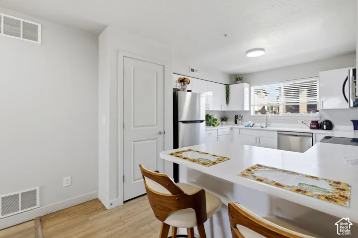 Kitchen featuring white gloss cabinetry, stone-finish countertops, stainless steel appliances, and wood-finish flooring