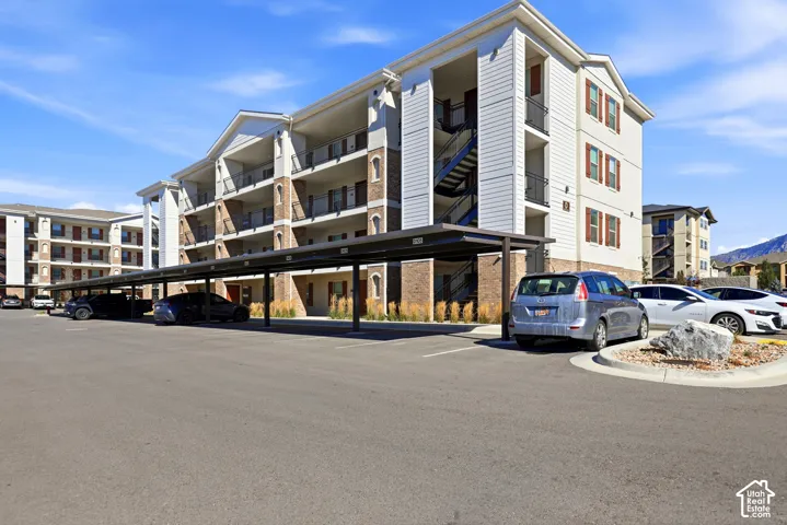 Multi-story building exterior featuring stone and horizontal siding, covered parking structures, private balconies, and concrete curb landscaping
