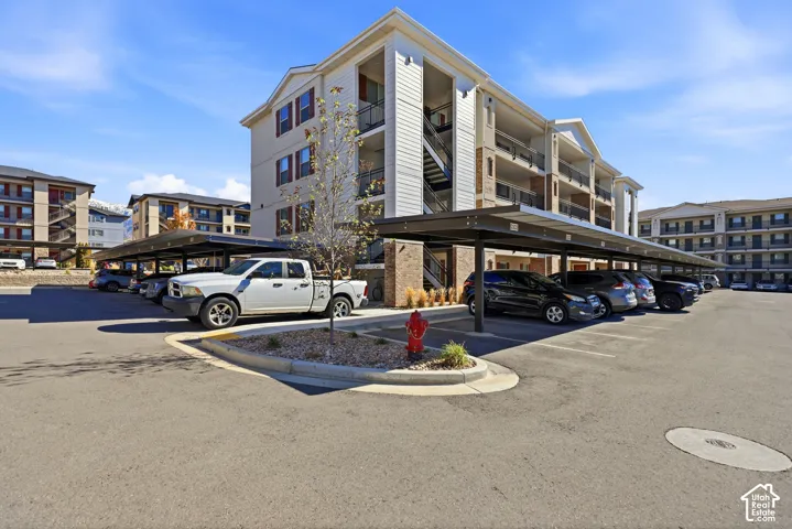 Multi-story building exterior with covered parking structures, horizontal siding, masonry accents, and private balconies