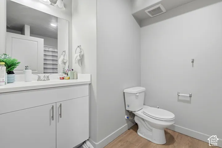 Bathroom featuring a white vanity cabinet, solid-surface countertop with an integrated sink, polished chrome faucet, wall-mounted mirror, and wood-finish flooring