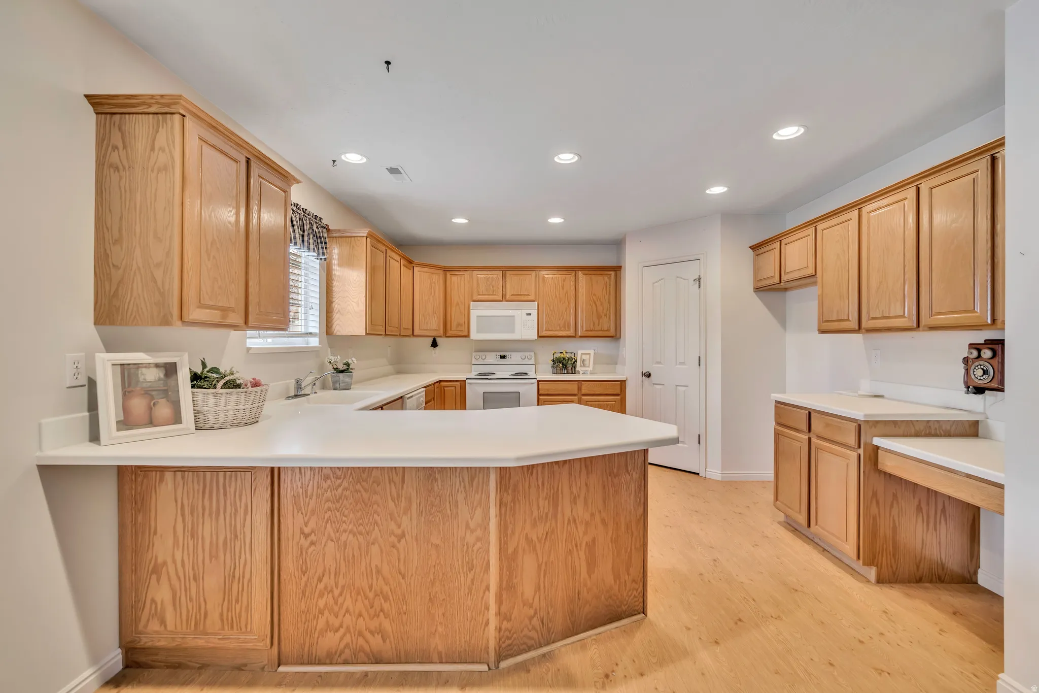 Kitchen featuring light countertops, white appliances, a peninsula, light wood finished floors, and recessed lighting