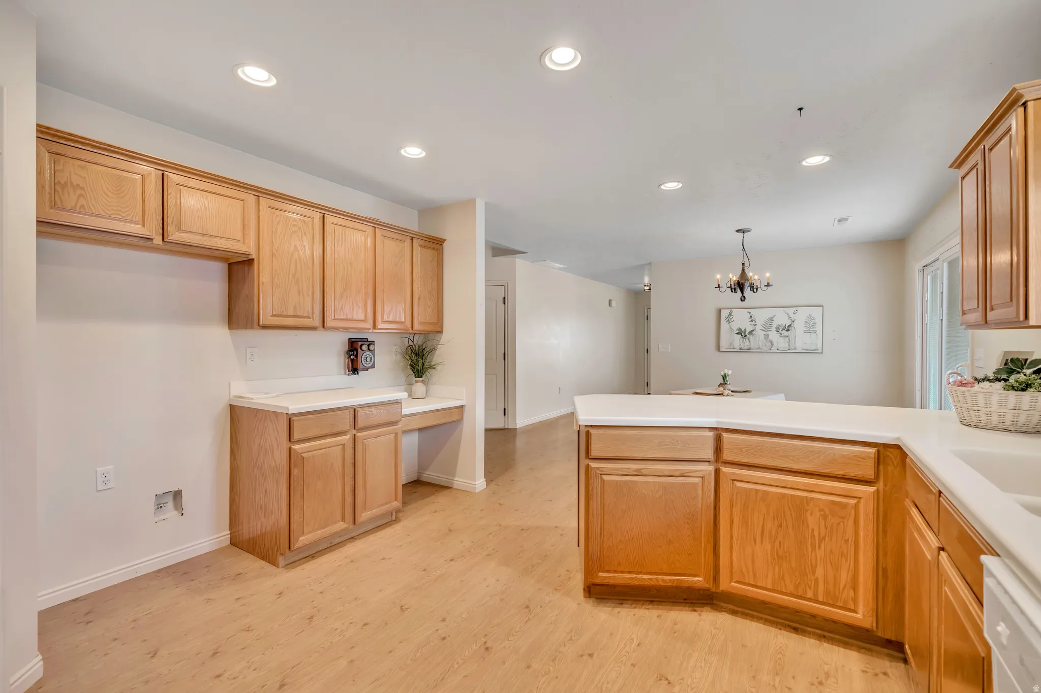 Kitchen with a peninsula, light countertops, suspended lighting, light wood finished floors, and white dishwasher