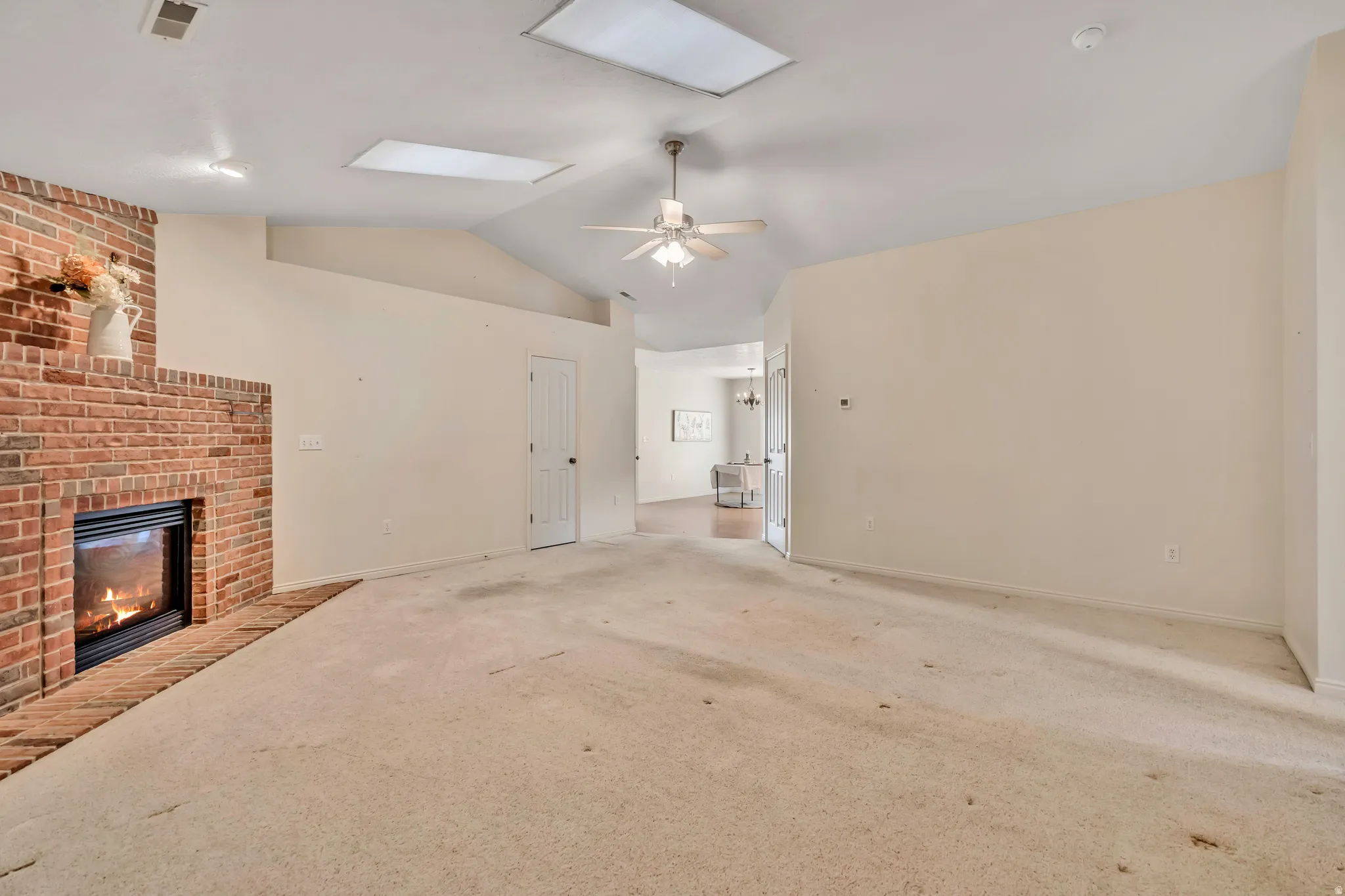 Unfurnished living room with carpet floors, ceiling fan, and a brick fireplace