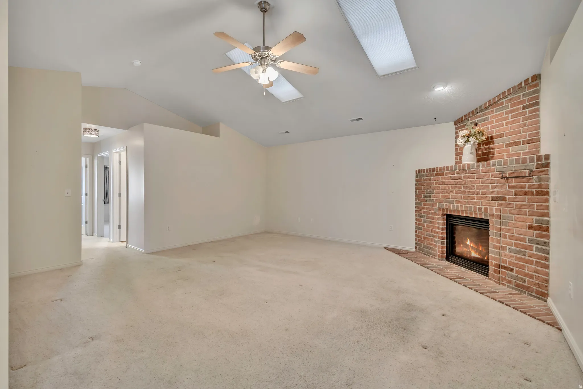 Unfurnished living room featuring a fireplace, ceiling fan, vaulted ceiling, light carpet, and a skylight