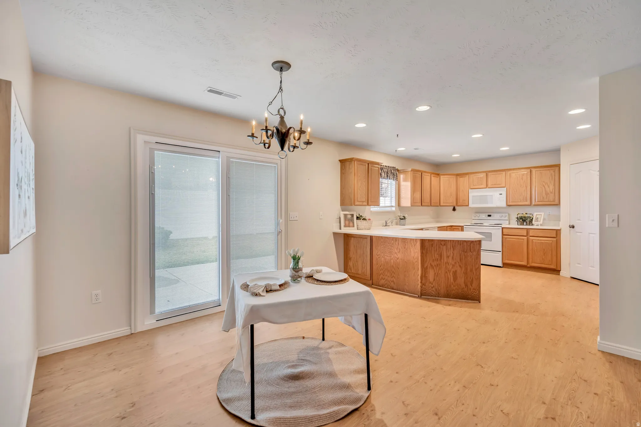 Kitchen with light countertops, white appliances, a peninsula, light wood-type flooring, and hanging lights