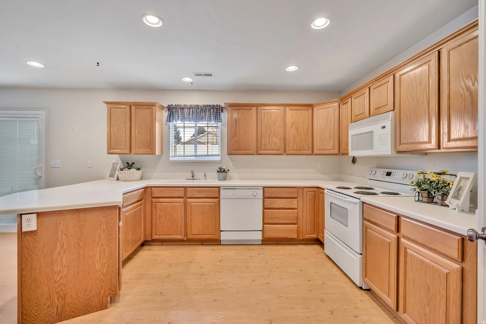 Kitchen with a peninsula, white appliances, light countertops, recessed lighting, and light wood finish cabinetry