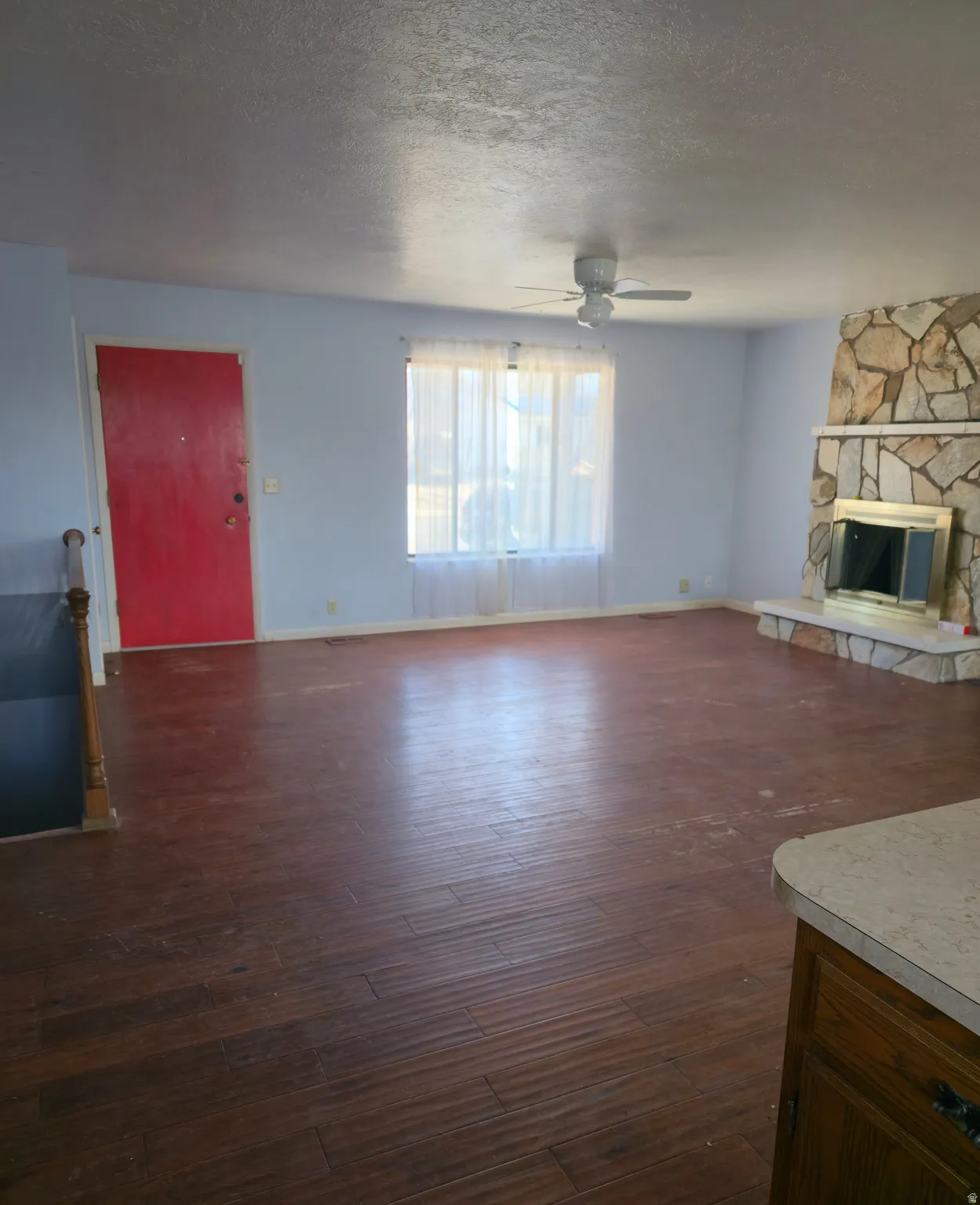 Unfurnished living room featuring a fireplace, ceiling fan, dark wood-style flooring, and a textured ceiling