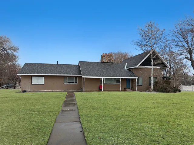 Ranch-style house featuring roof with shingles, a front yard, covered porch, a chimney, and stucco siding