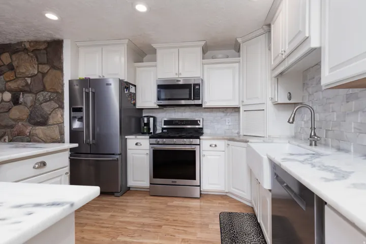 Kitchen featuring stainless steel appliances, light wood-type flooring, white cabinets, backsplash, and a textured ceiling
